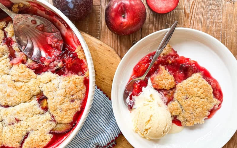 Plum cobbler being served with a large spoon.