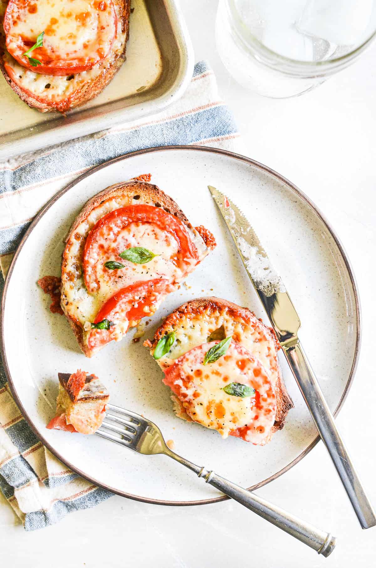 tomato melts with bubbly cheese topping on a plate.