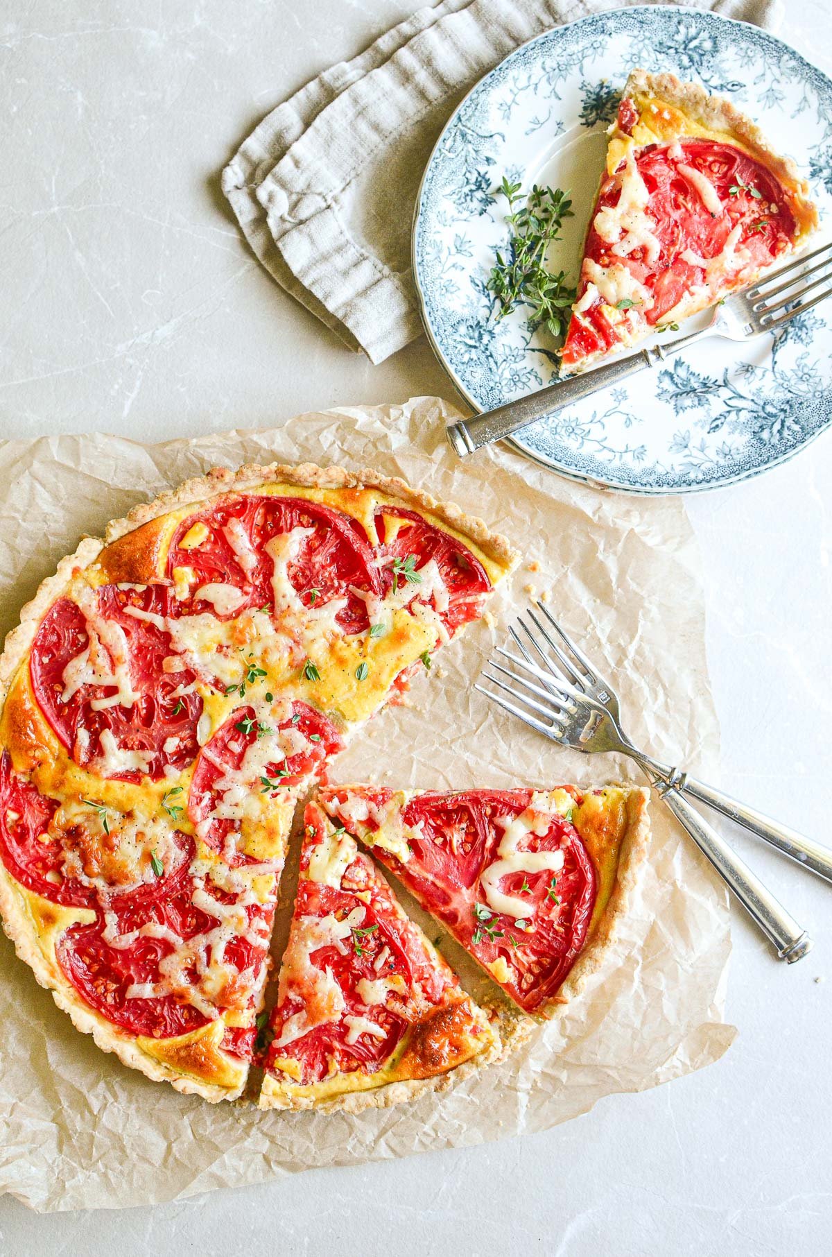 tomato tart on parchment paper, with a slice on a plate.