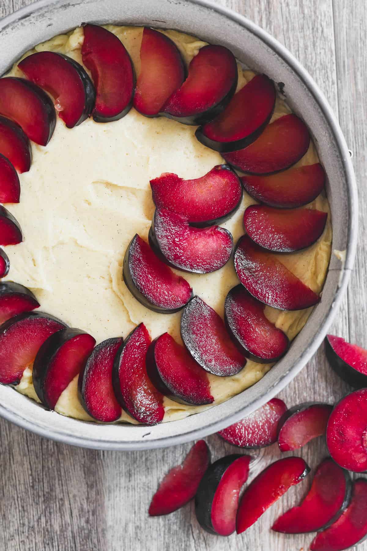 arranging plum slices on a cardamom plum cake.