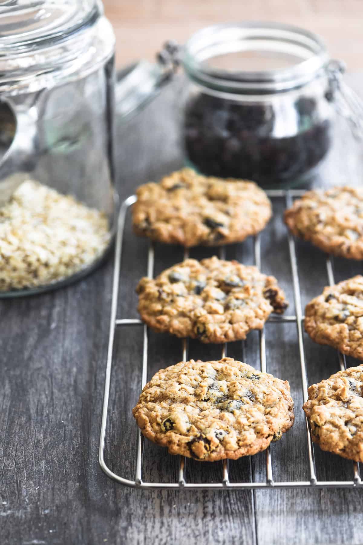 oatmeal raisin cookies cooling on a rack with a jar of oats and raisins in the background.