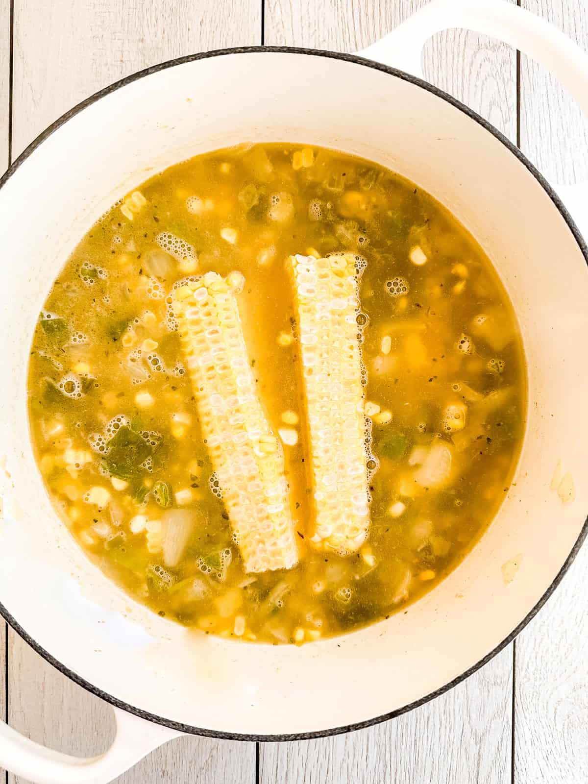 making white chicken chili in a Dutch oven with corn cobs in the broth.