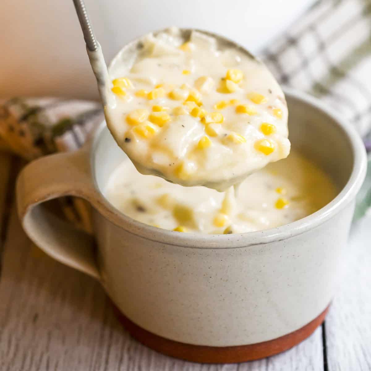 Ladling corn and cheddar cheese chowder into a mug.