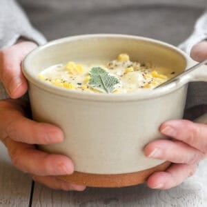 holding a mug of corn and cheddar cheese chowder.