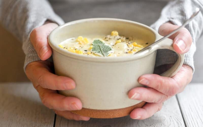 holding a mug of corn and cheddar cheese chowder.