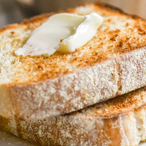 Toasting white bread topped with butter, on a plate.