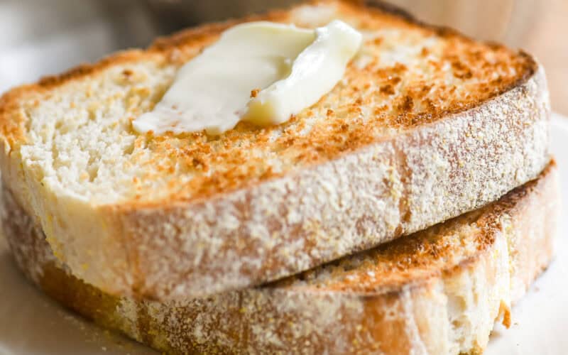 Toasting white bread topped with butter, on a plate.
