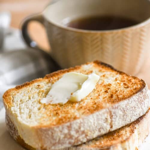 Two slices of toasting white bread toasted on a plate with butter.