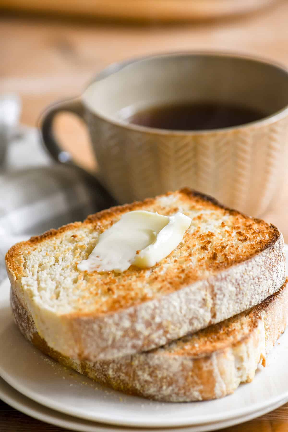 Two slices of toasting white bread toasted on a plate with butter.
