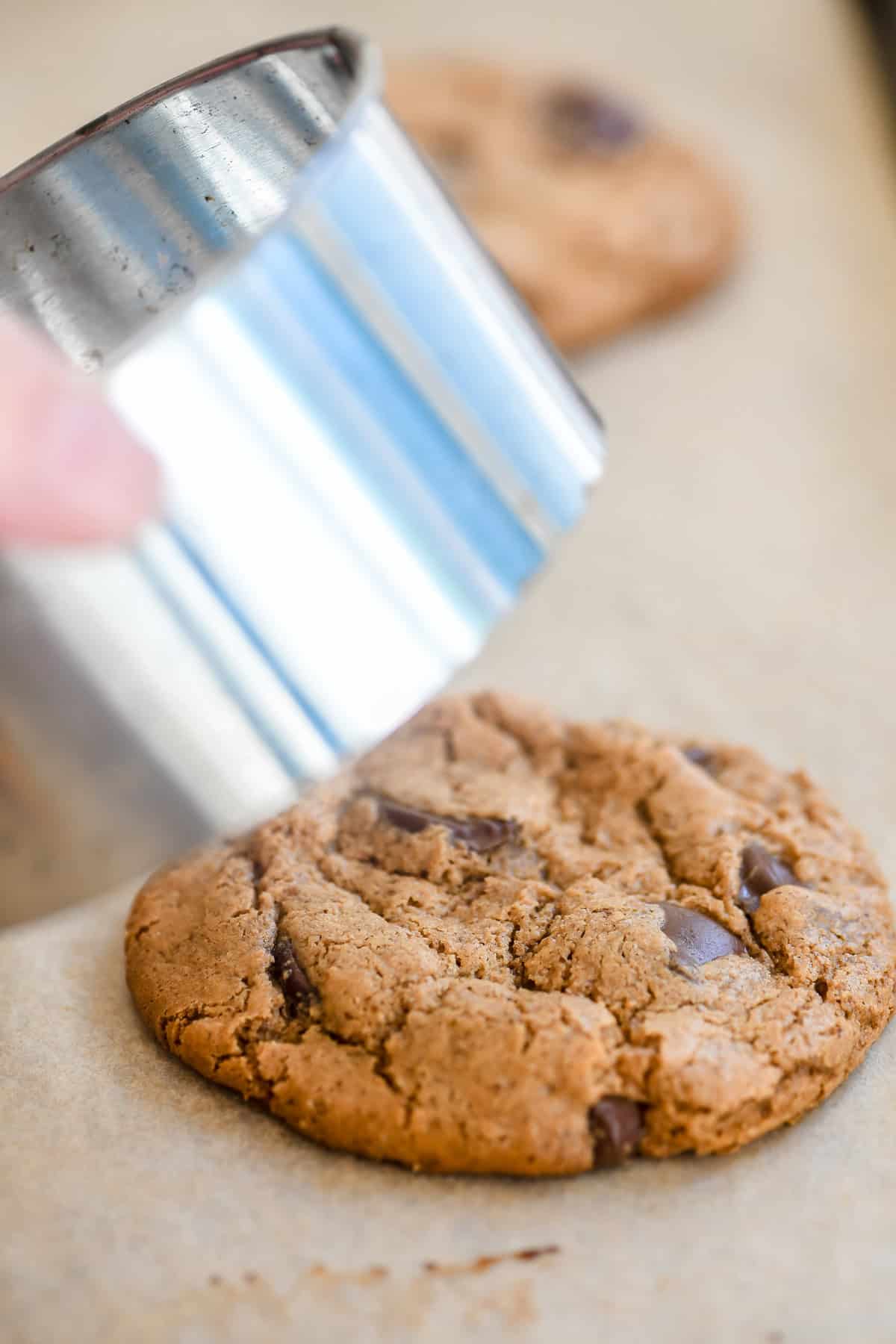 Scooting a baked flourless almond butter cookie round with a cookie cutter.
