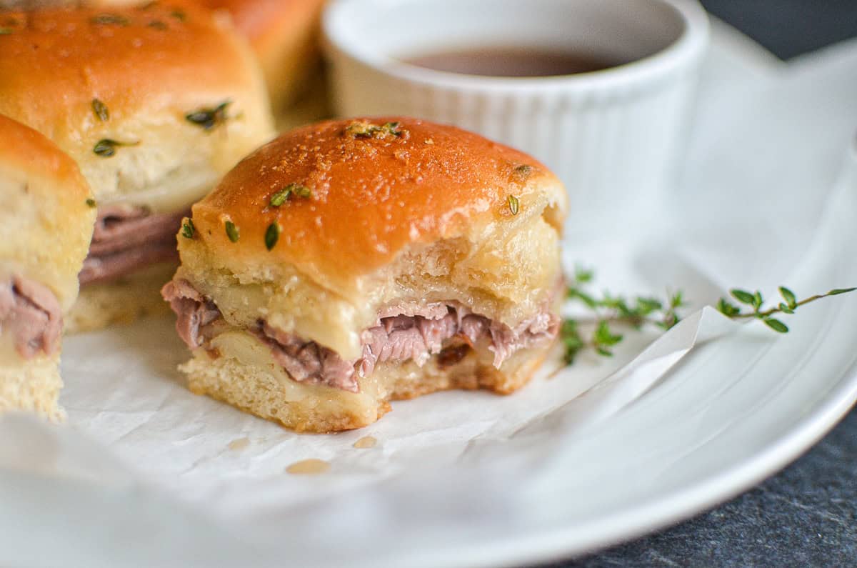 A French dip slider with a bite taken out, on a white platter.