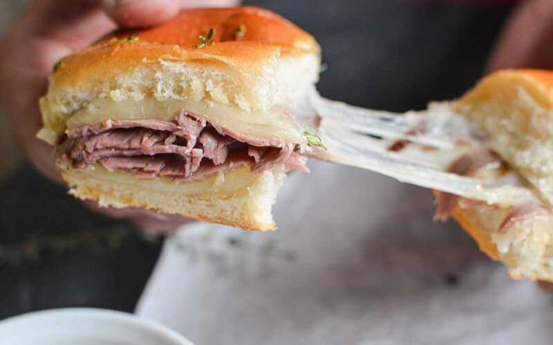 pulling apart a French dip slider with gooey melted cheese.