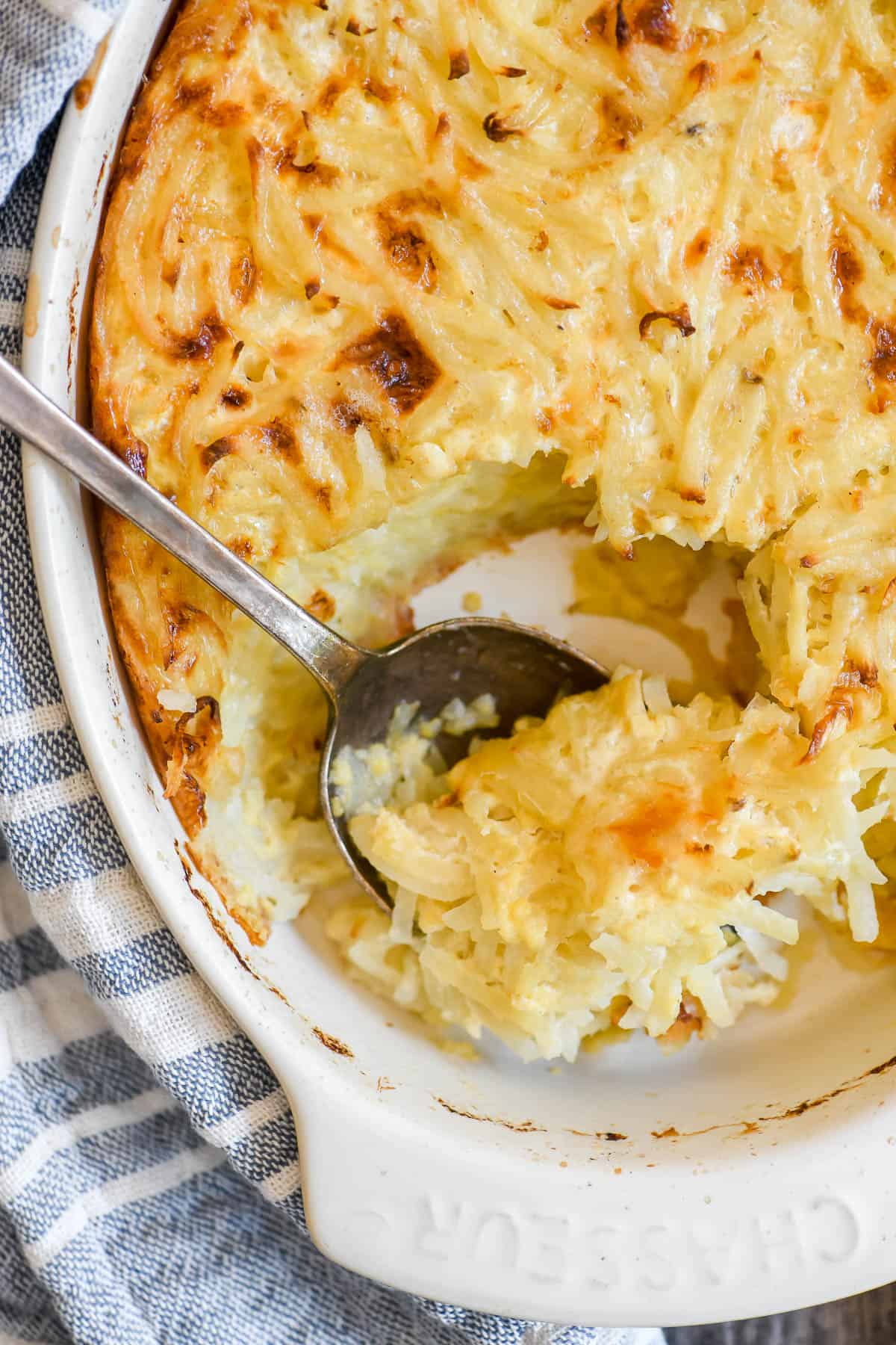 Serving grated potato casserole with silver spoon.