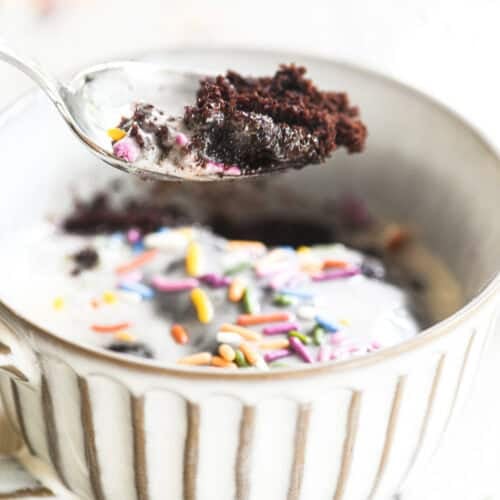 Taking a bite of a chocolate mug cake topped with frosting and sprinkles