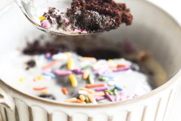 Taking a bite of a chocolate mug cake topped with frosting and sprinkles