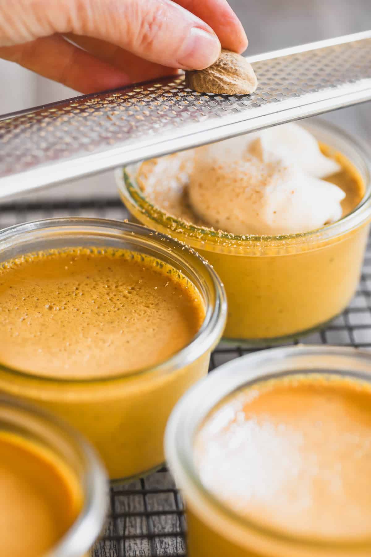 Grating fresh nutmeg on pumpkin pot de creme in small Weck jars.