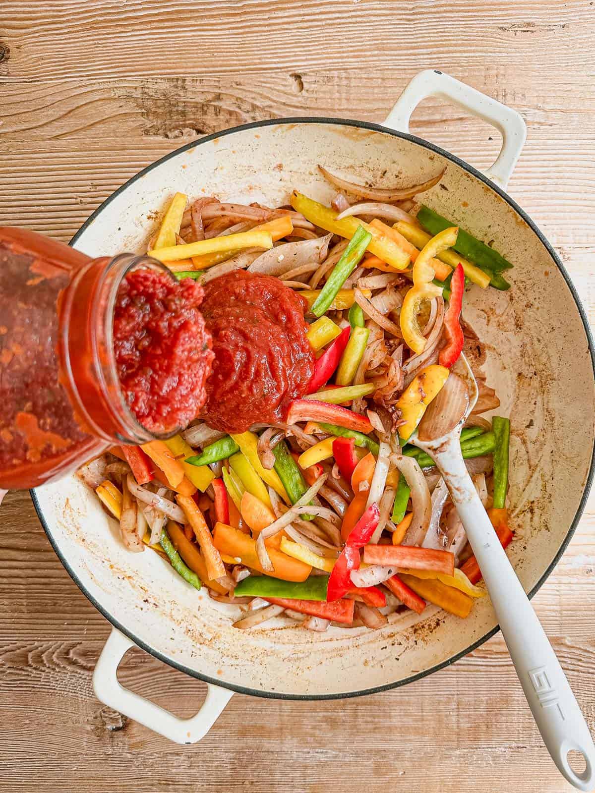 adding tomato sauce to pan for sausage and peppers