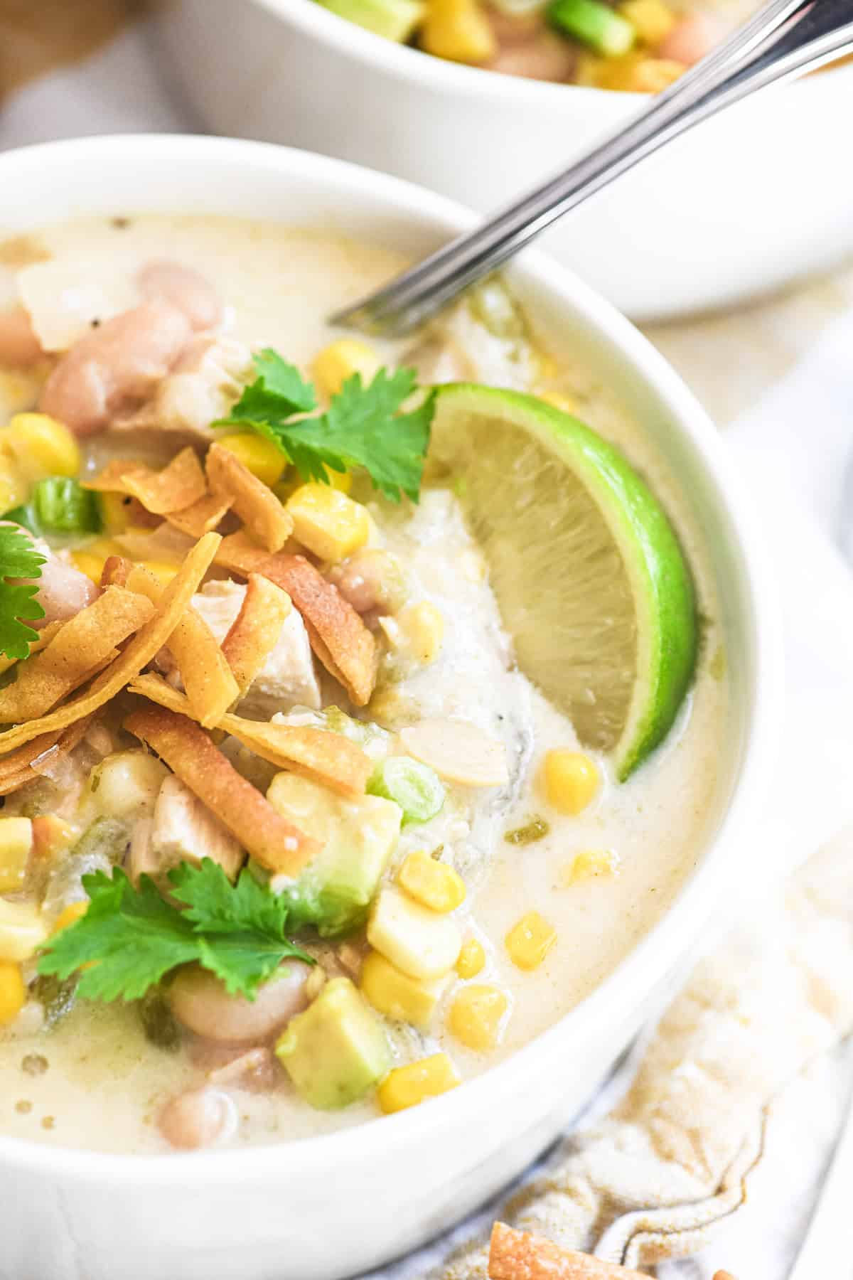 white chicken chili in a bowl topping with cilantro, avocados, and fried tortilla strips.