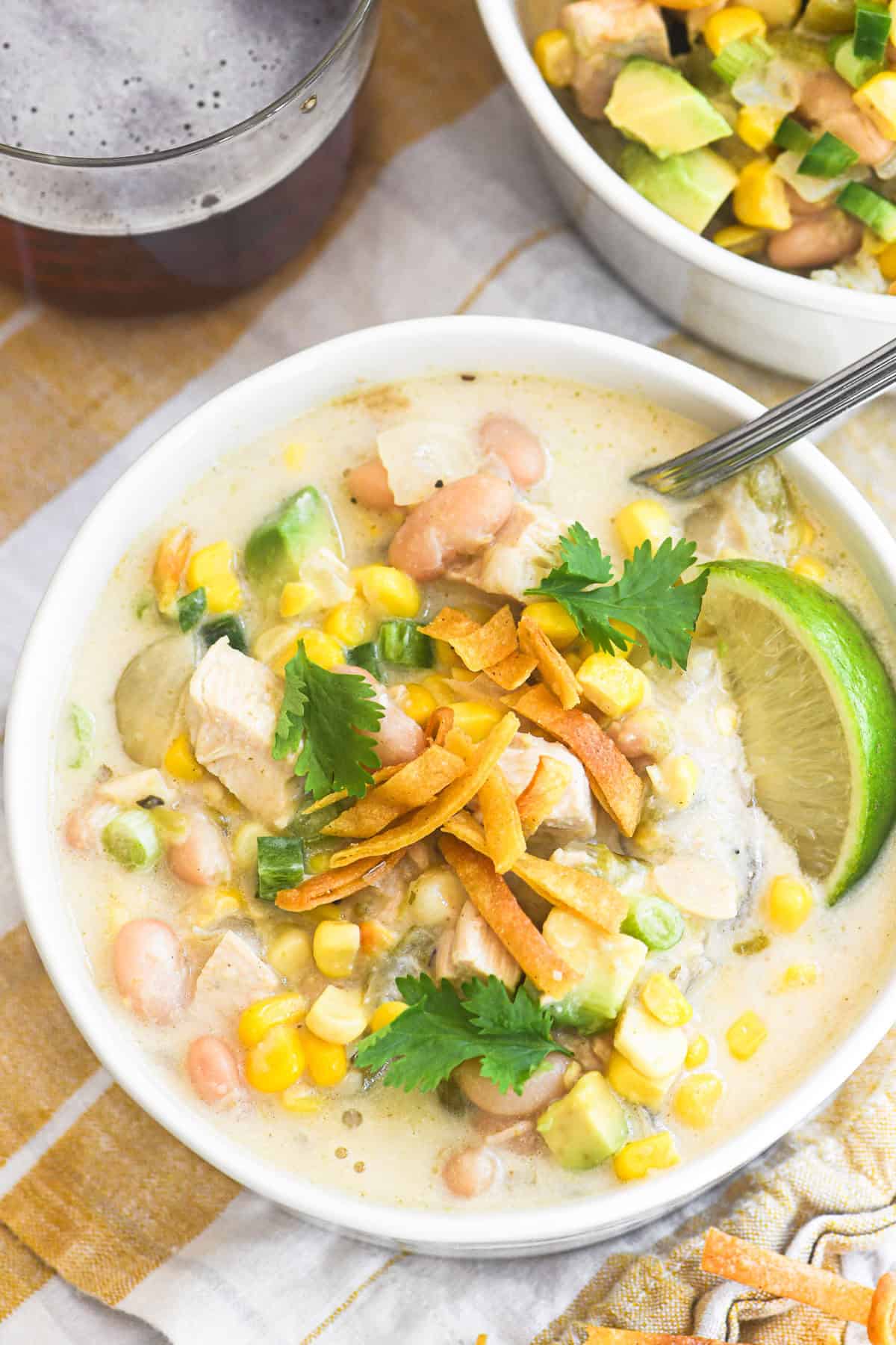 a bowl of white chicken chili topped with avocado and tortilla strips.