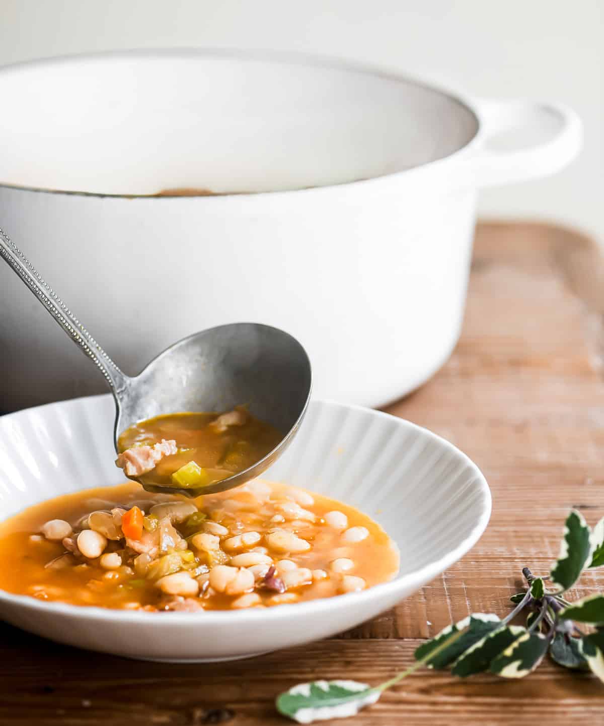 ladling white bean and bacon soup into bowl.