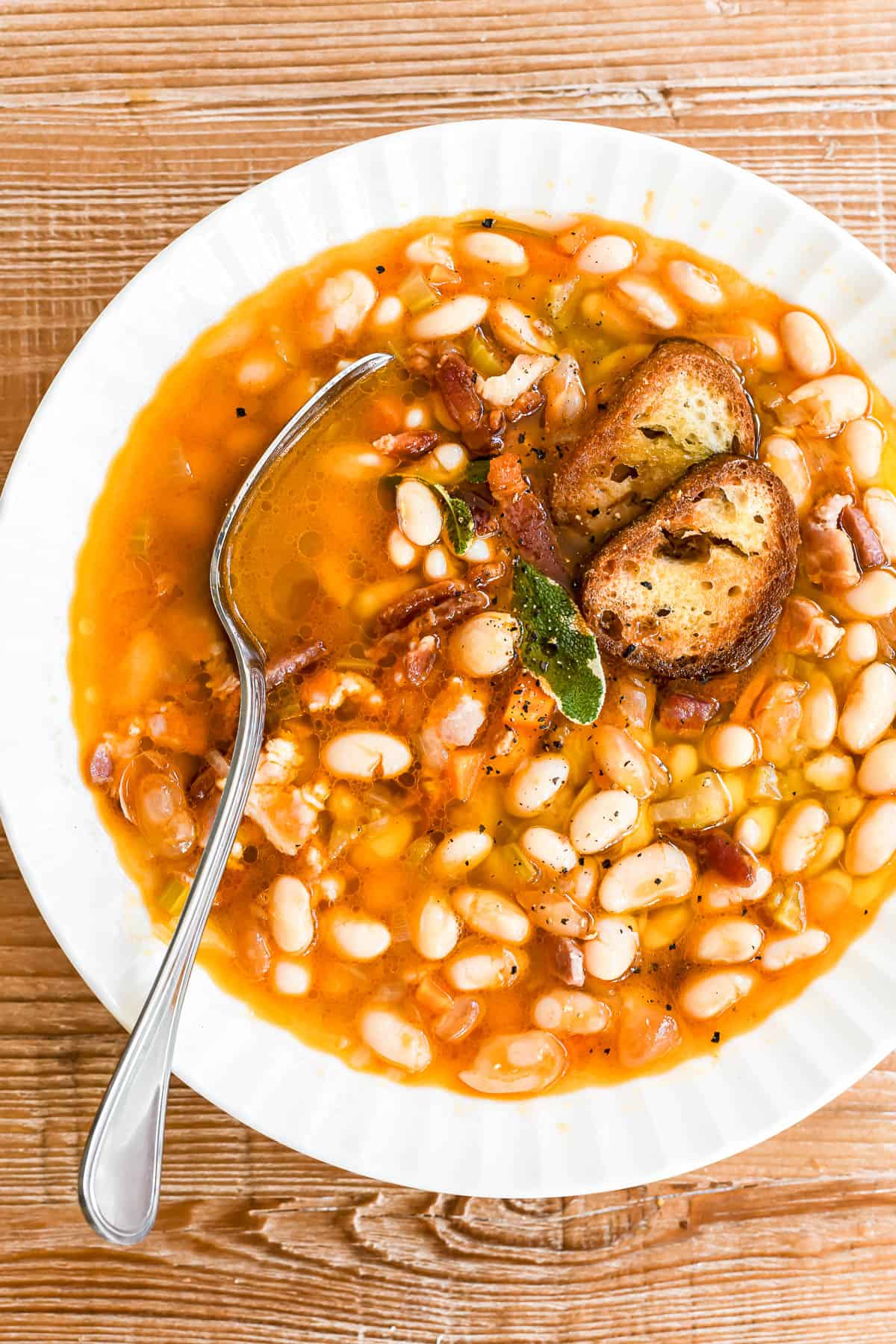 a bright bowl of white bean and bacon soup, with croutons and sage leaves.