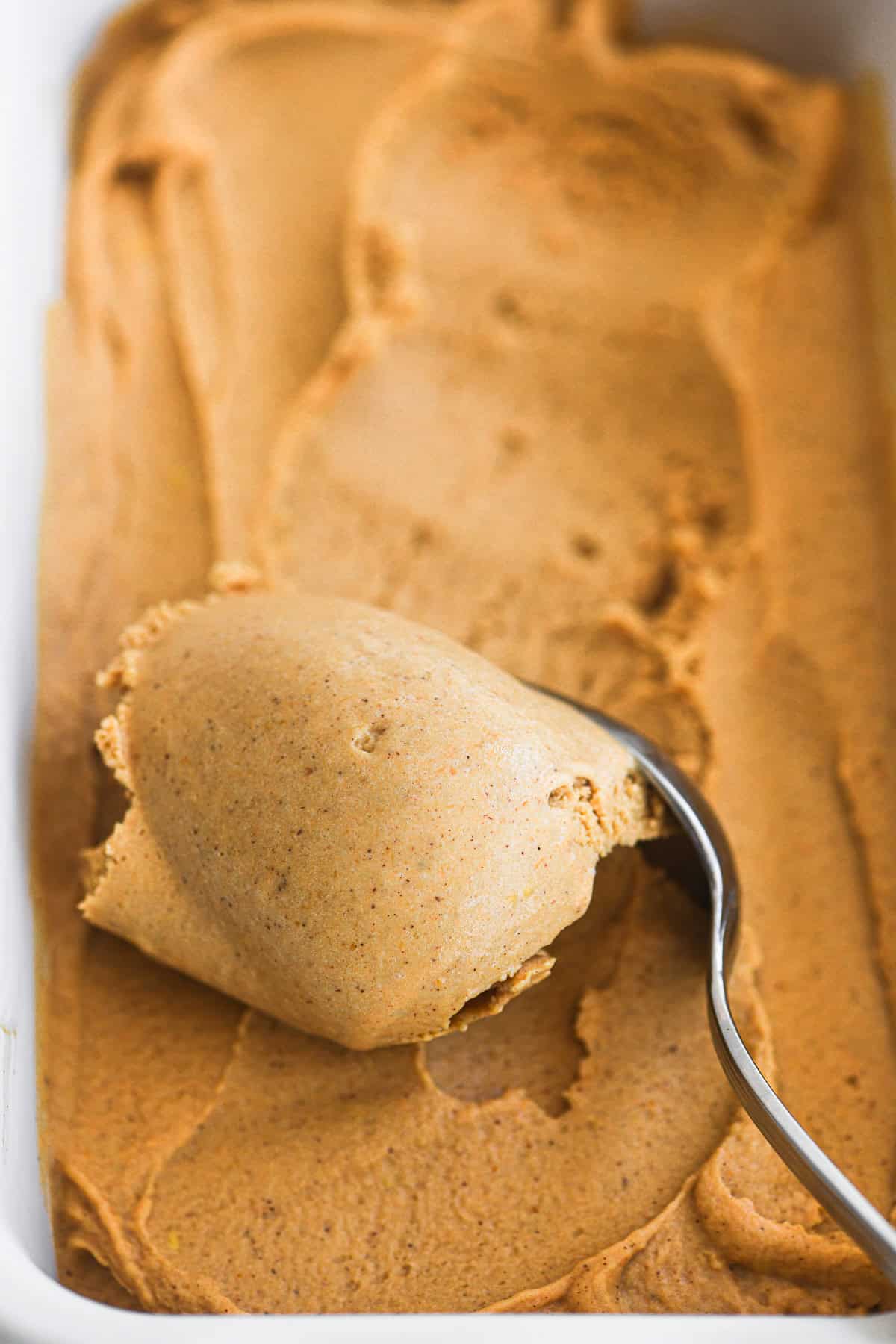 Scooping just made pumpkin ice cream with a spoon.