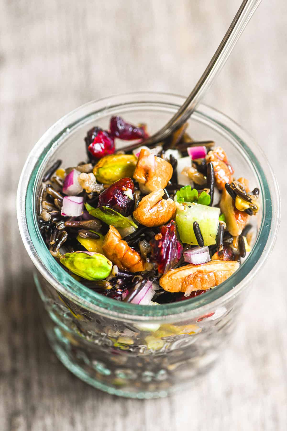 colorful wild rice salad with cranberries in a glass jar with spoon.