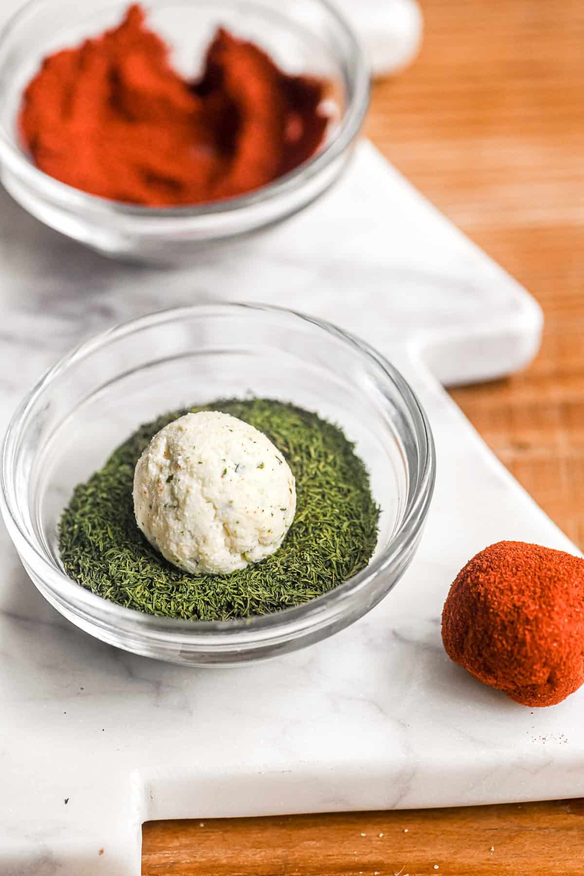 A Boursin mini cheese ball, in a small bowl of dried dill.