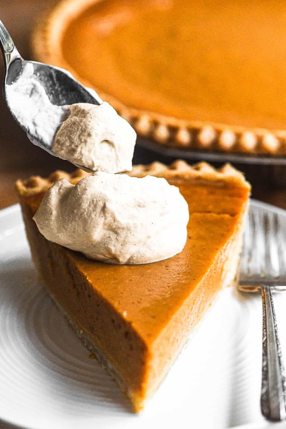 dolloping flavored whipped cream on a slice of pumpkin pie