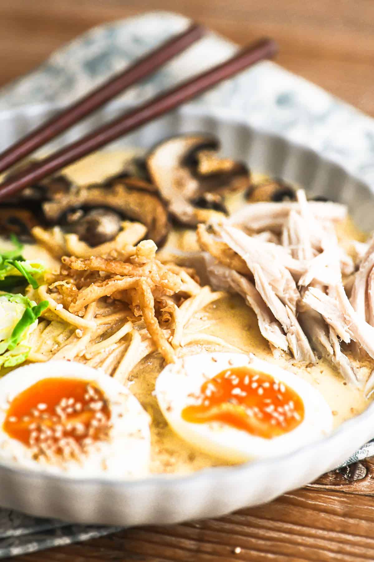 chopsticks in a bowl of creamy ramen with turkey and ramen eggs.