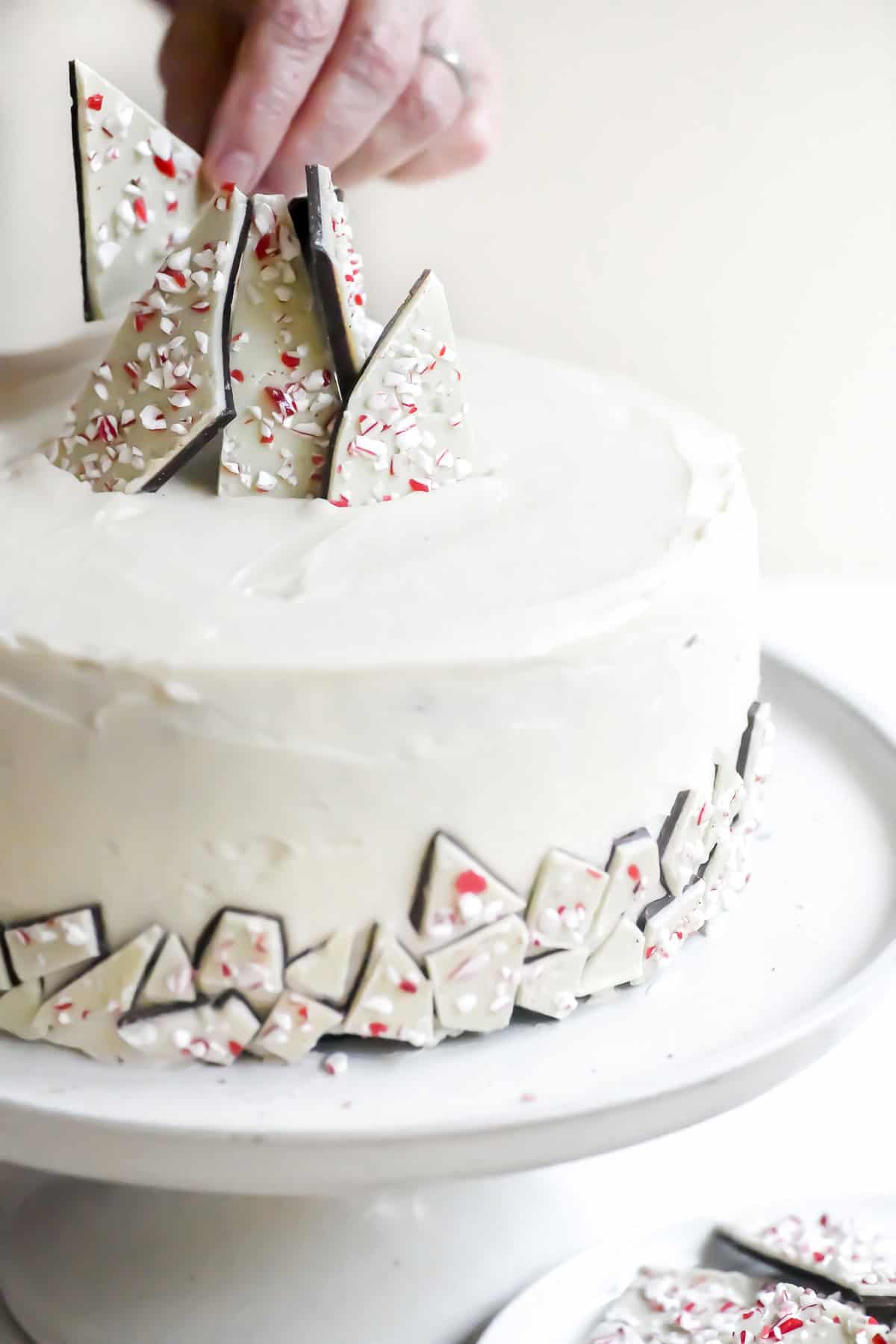 Placing peppermint bark shards on top of a peppermint bark layer cake.