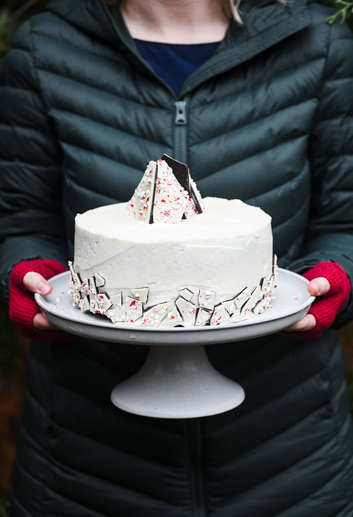 Girl holding a peppermint bark cake on a cake stand.
