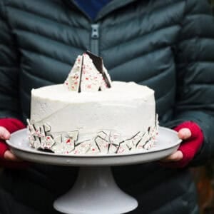 Holding a peppermint bark Christmas Cake on a cake platter.