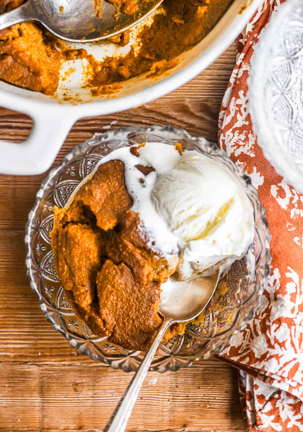 pumpkin Indian pudding in a glass bowl with ice cream.