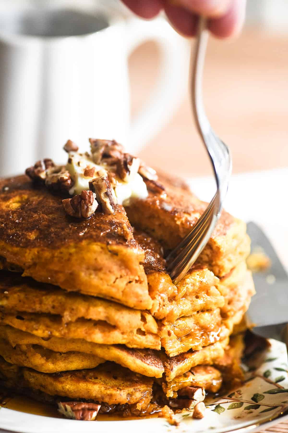 Taking a bite from a stack of 4 pumpkin panckes with syrup.