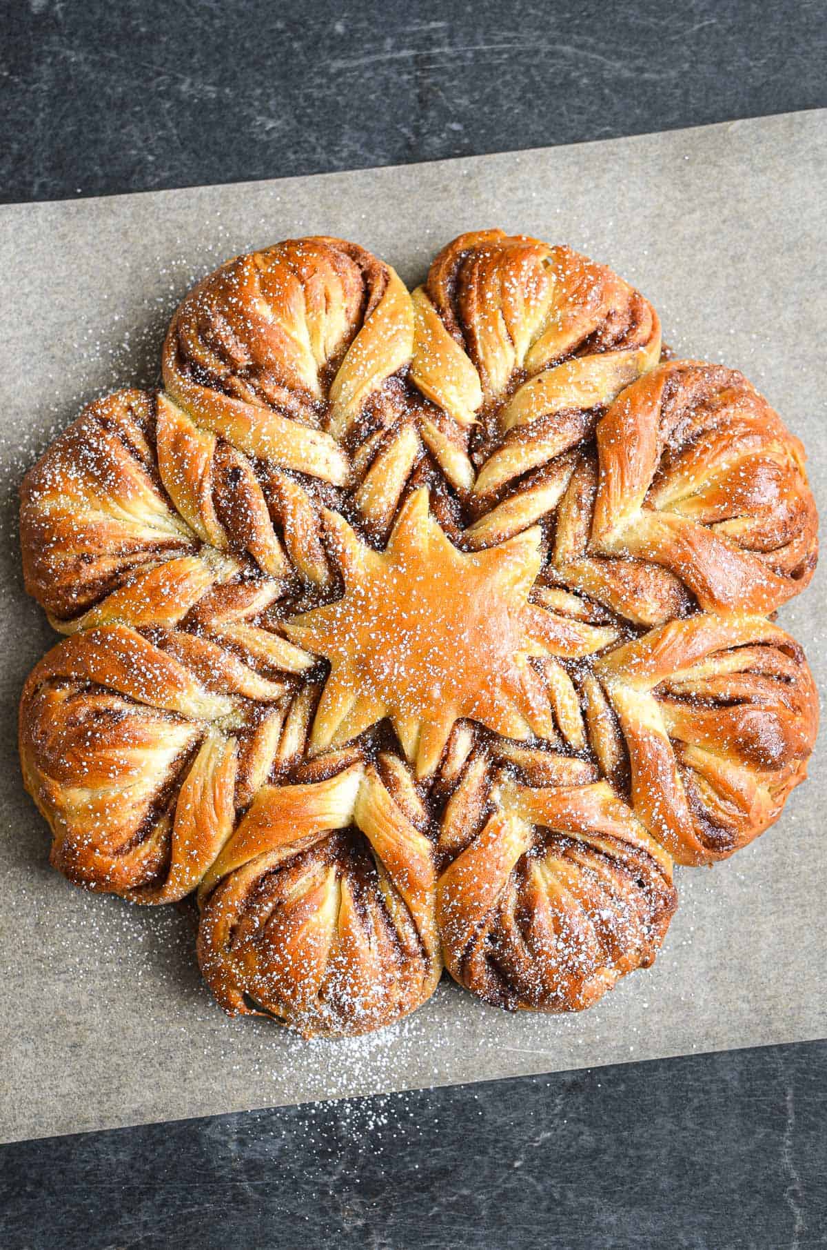 just baked cinnamon star bread on parchment paper, with a light dusting of powdered sugar.