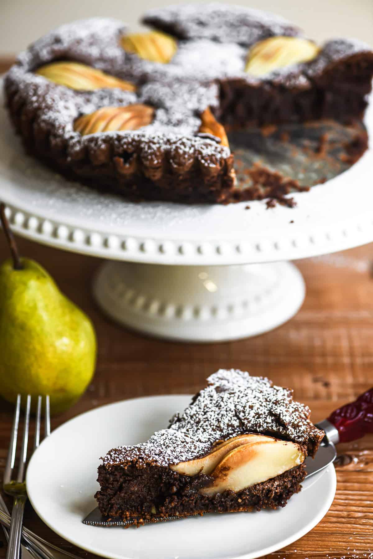gluten free chocolate almond pear cake on a cake stand, with piece in foreground.