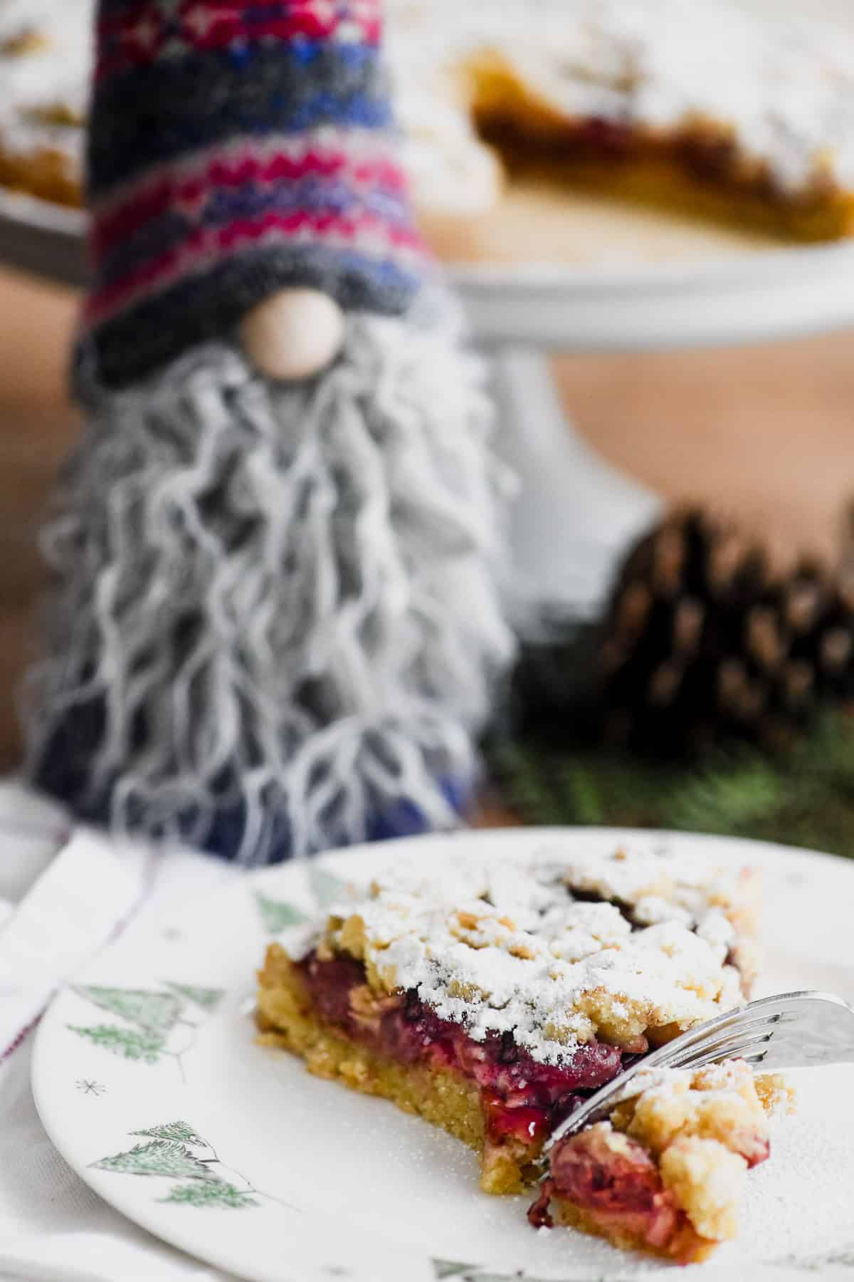 sour cherry streusel cake on a plate with fork and Christmas gnome looking on.