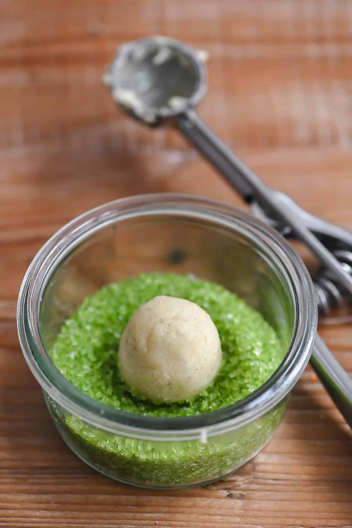 A ball of sugar cookie dough in a bowl of sprinkles.