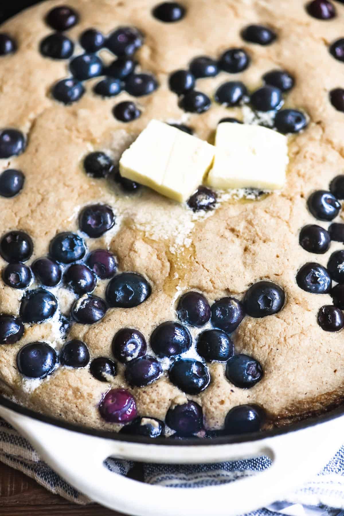 overhead look at a blueberry skillet pancake with melting pats of butter.