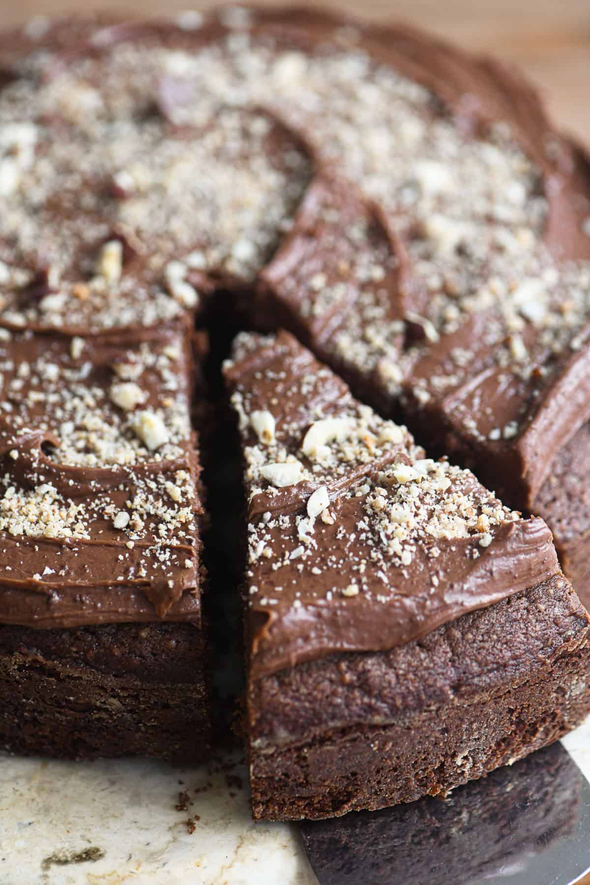 removing a slice of dark chocolate hazelnut cake with a cake server.