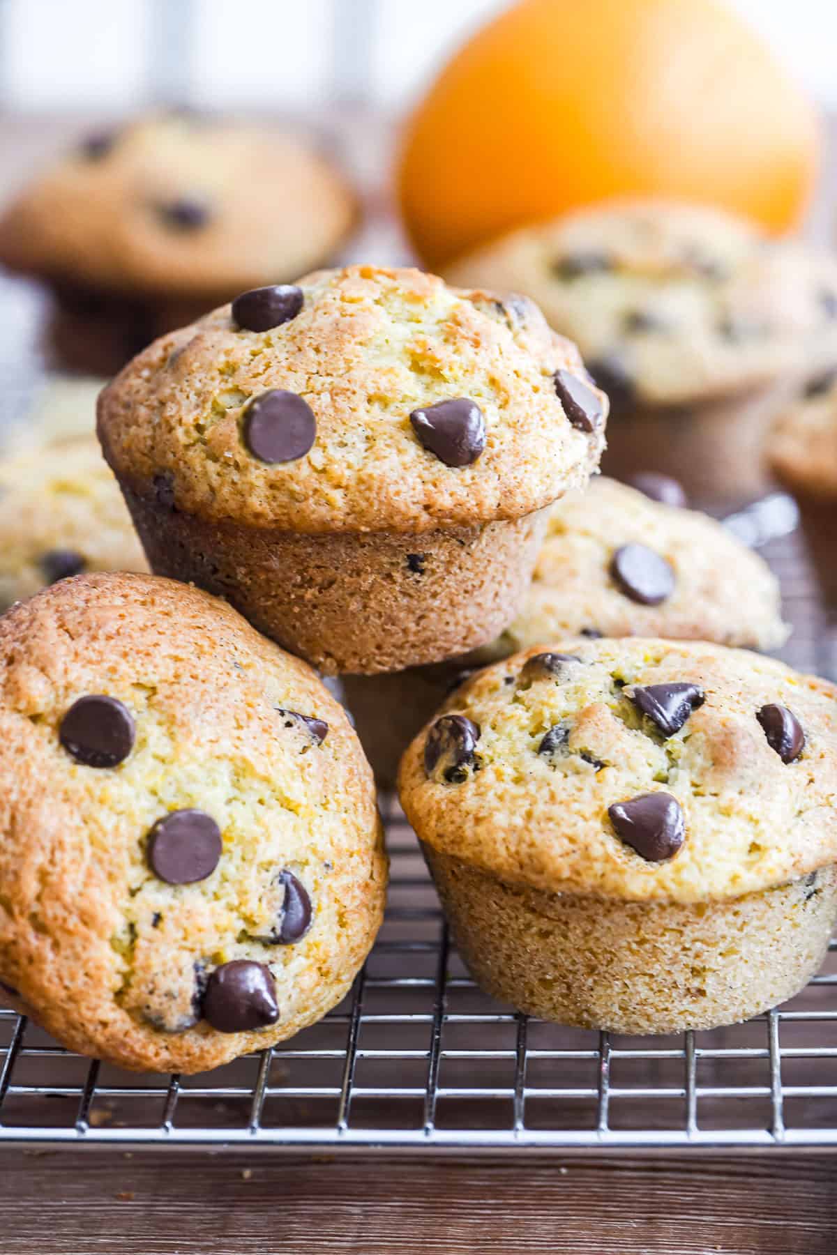 orange chocolate chip muffins piled on a rack. 