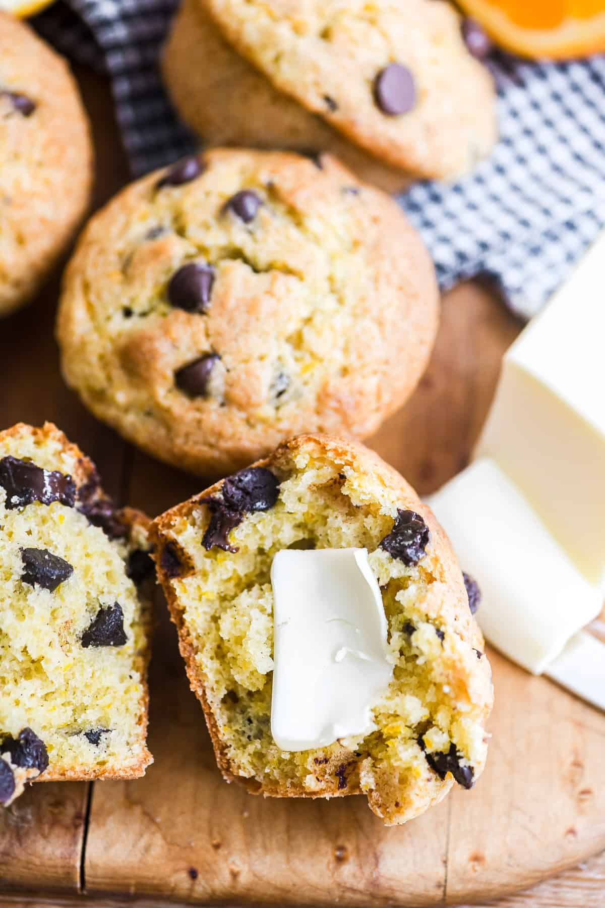 orange chocolate chip muffins with one broken open to show texture, with butter.