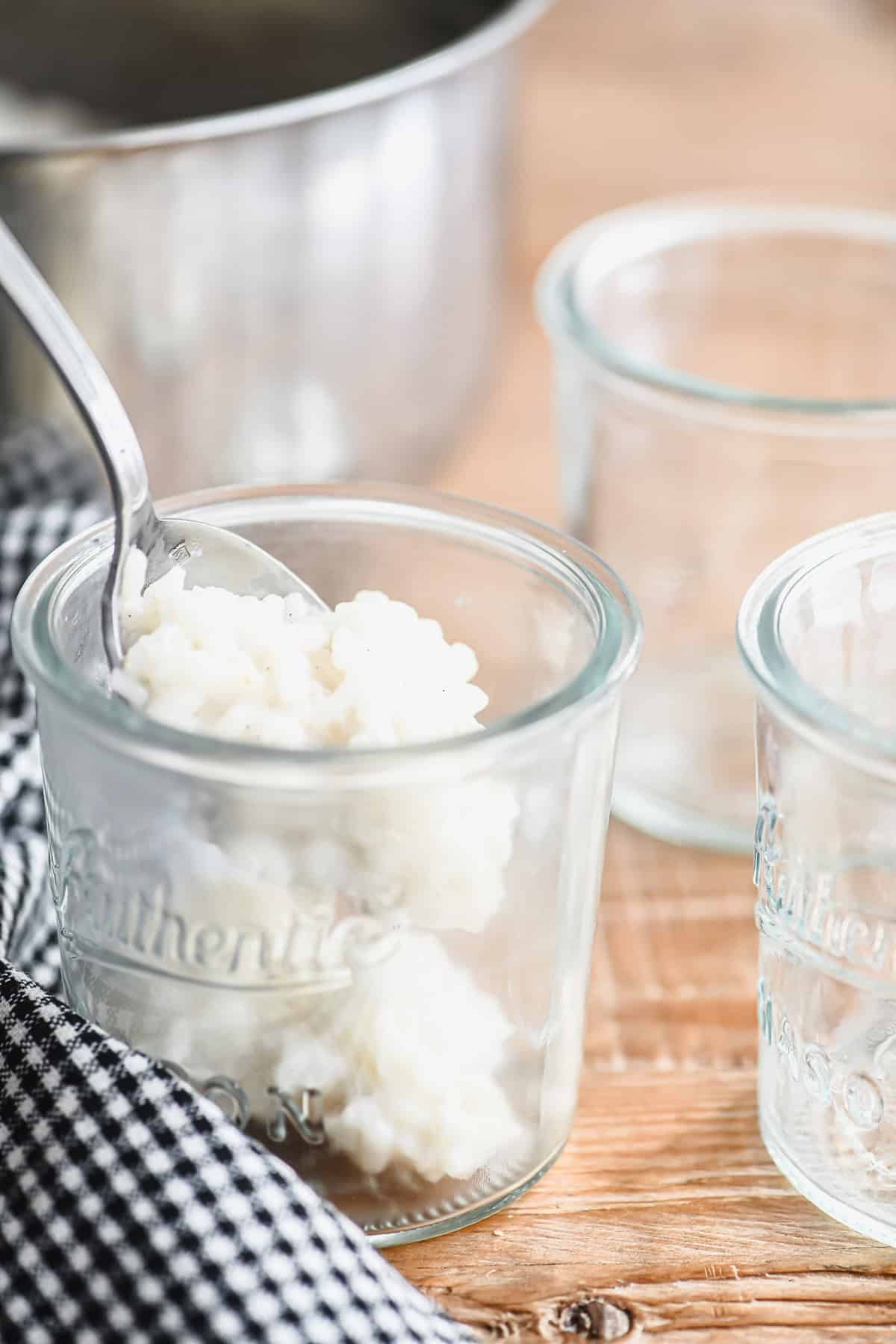 Spooning freshly made coconut rice pudding into small serving glasses.
