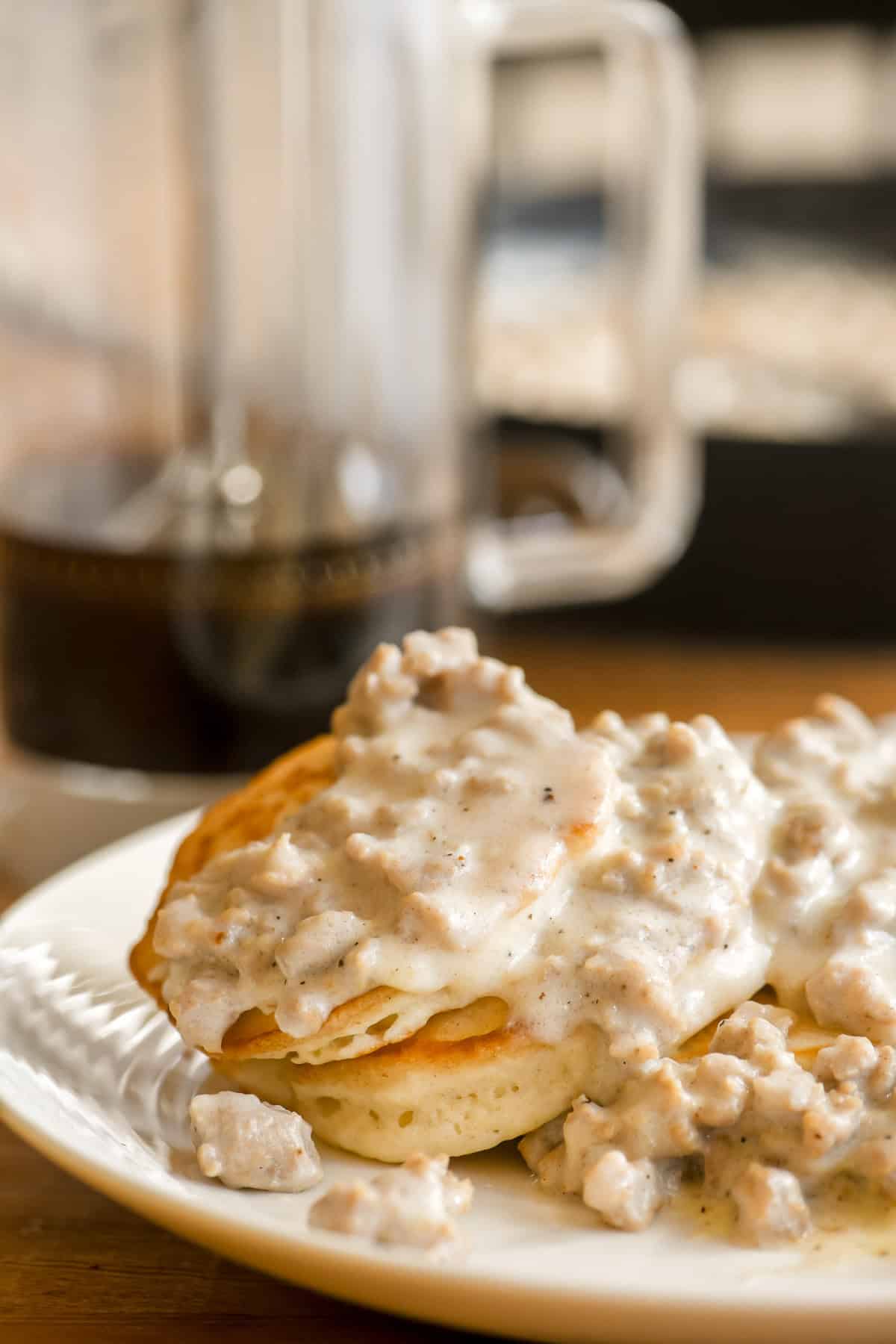 A plate of biscuit pancakes with country gravy, with coffee pot in the background.
