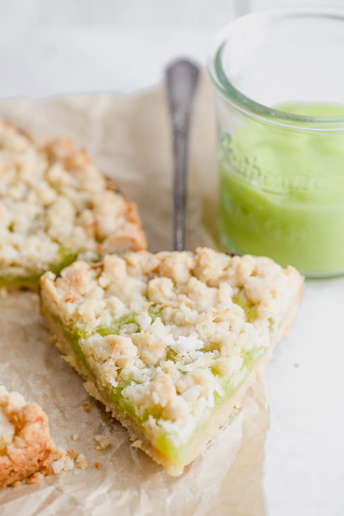 a slice of coconut lime shortbread tart with lime curd in background.
