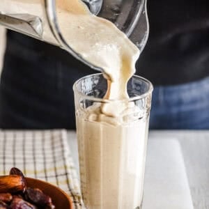 Pouring a thick date shake smoothie into a glass.