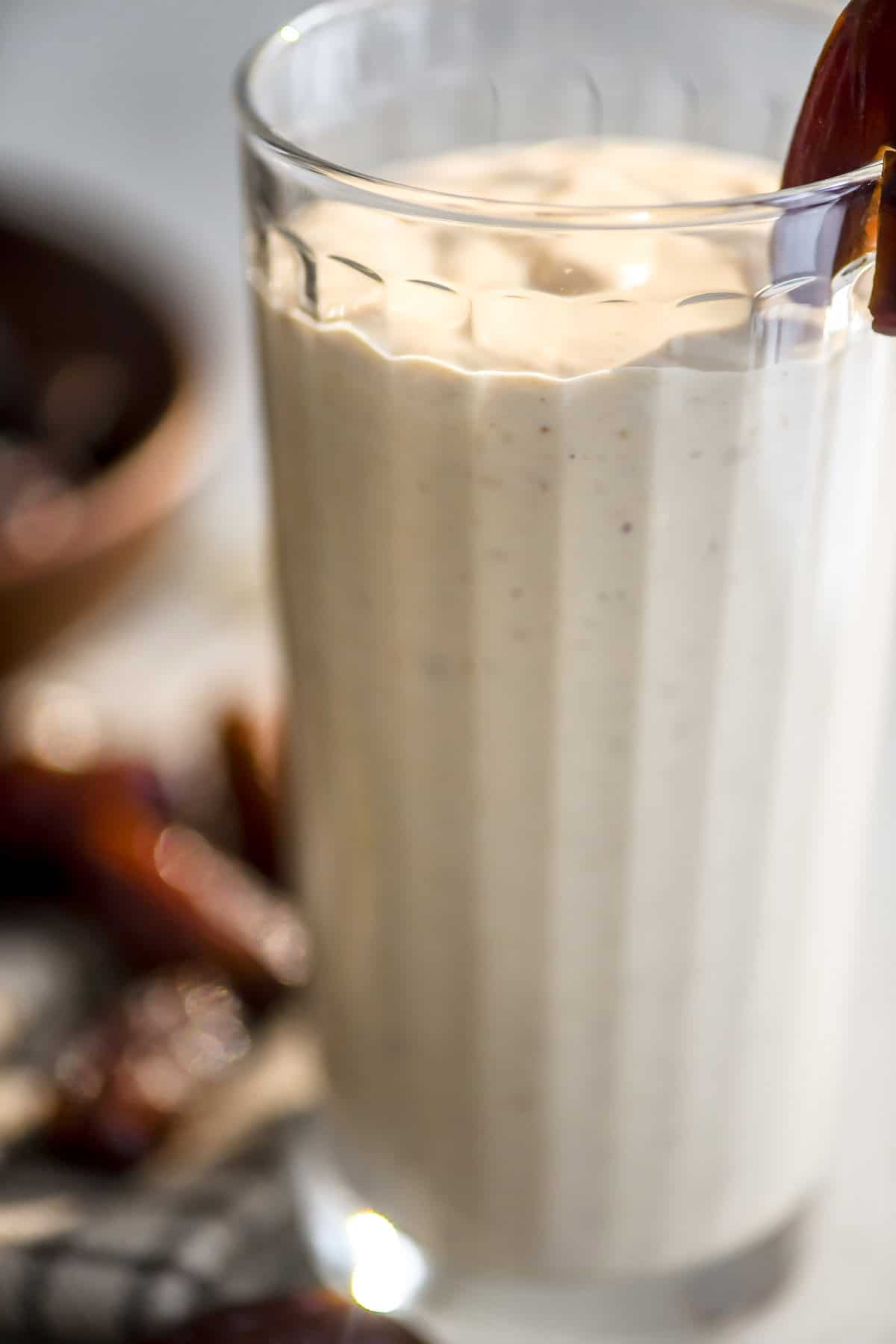 close look at a thick and creamy date shake smoothie in a ribbed glass.