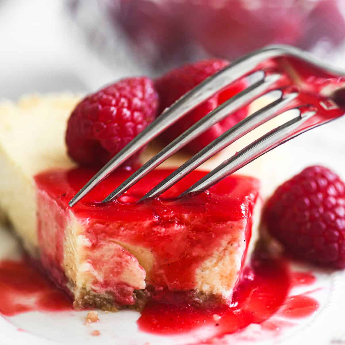 Taking a bite of a slice of fromage blanc cheesecake topped with raspberry coulis.