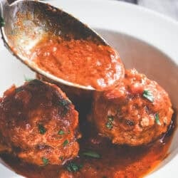 spooning marinara sauce onto Italian Ricotta Meatballs.